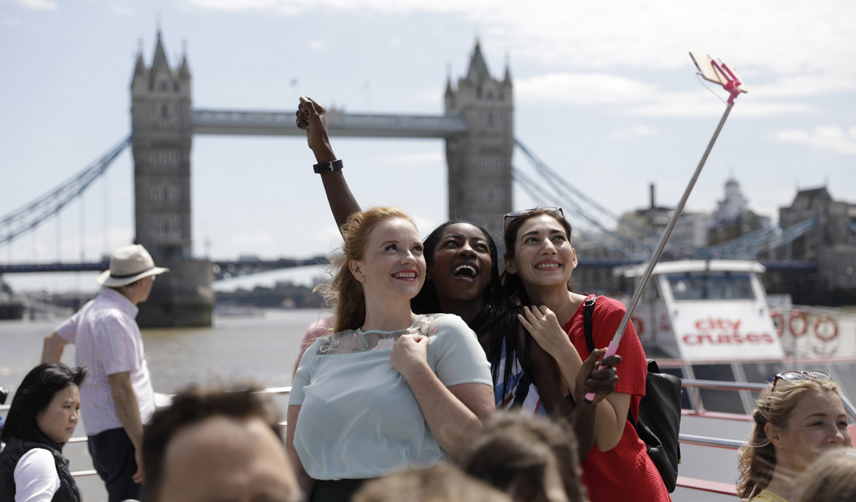 Three girls take a selfie on board CIty Cruises in front of Tower Bridge